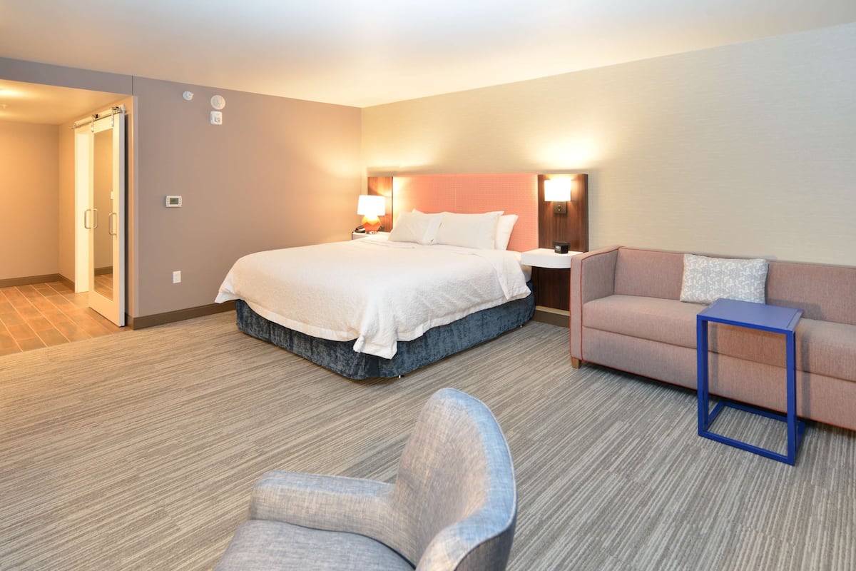A hotel room with a bed, a sofa, a chair, and a small table.