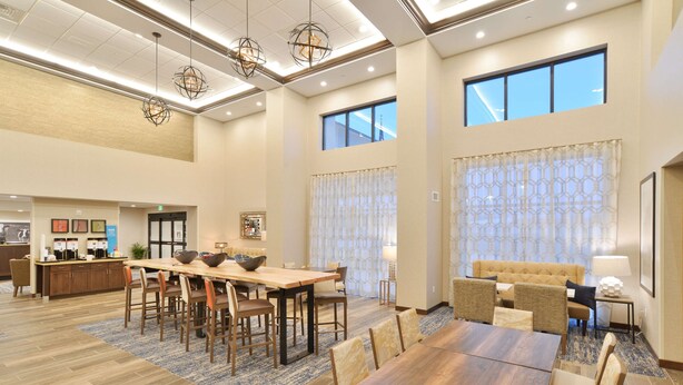 A spacious hotel dining area with a long wooden table and chairs, a sofa set, and a bar area in the background.