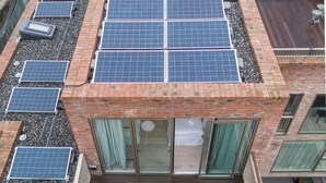 Um edifício com diversos painéis solares no telhado e uma varanda com uma pequena mesa e cadeiras.