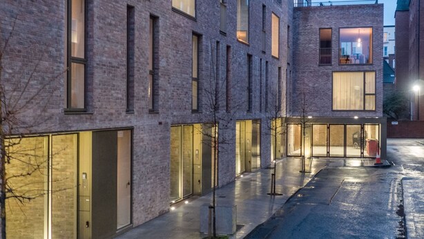 Um edifício moderno com grandes portas e janelas de vidro, um calçada pavimentada e um veículo estacionado.