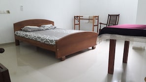 A bedroom with a wooden bed, a small table with a lace tablecloth, a chair, and a wall-mounted shelf. - Rooms One Five Four (Seeduwa - Katunayake)