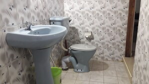 Een badkamer met een wastafel, toilet en groene afvalbak.