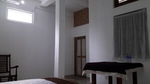 Een kamer met een bed, een tafel met een donkere tafelkleed, een raam met dunne gordijnen en een deur.