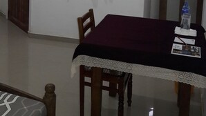 Een eethoek met een tafel, stoelen, een kantgordijn en een raam met jaloezieën.
