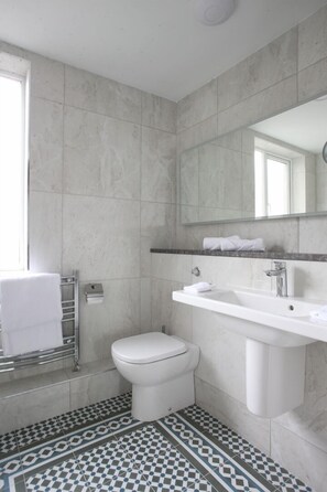 A bathroom with a white toilet, a sink with a mirror above it, and a patterned floor. - Hayes Hotel (Thurles)
