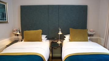 A hotel room with two beds, a large grey headboard, bedside tables with lamps, and a small nightstand with a phone.