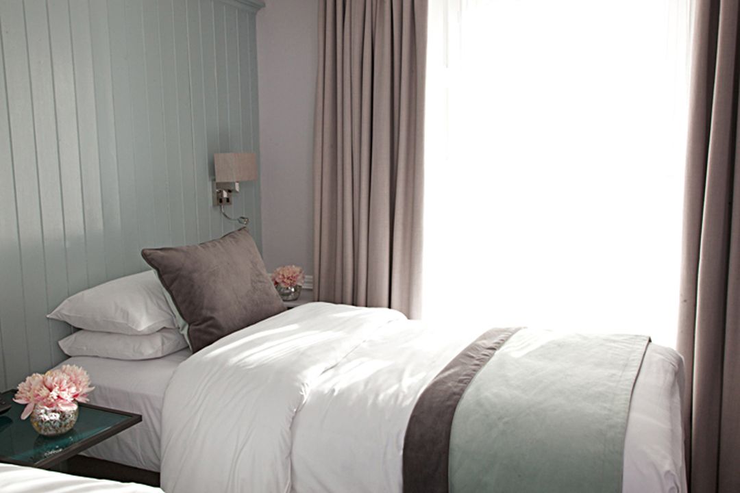 Una cama bien hecha con ropa de cama blanca y marrón, una mesita de noche con un florero y una lámpara de pared.