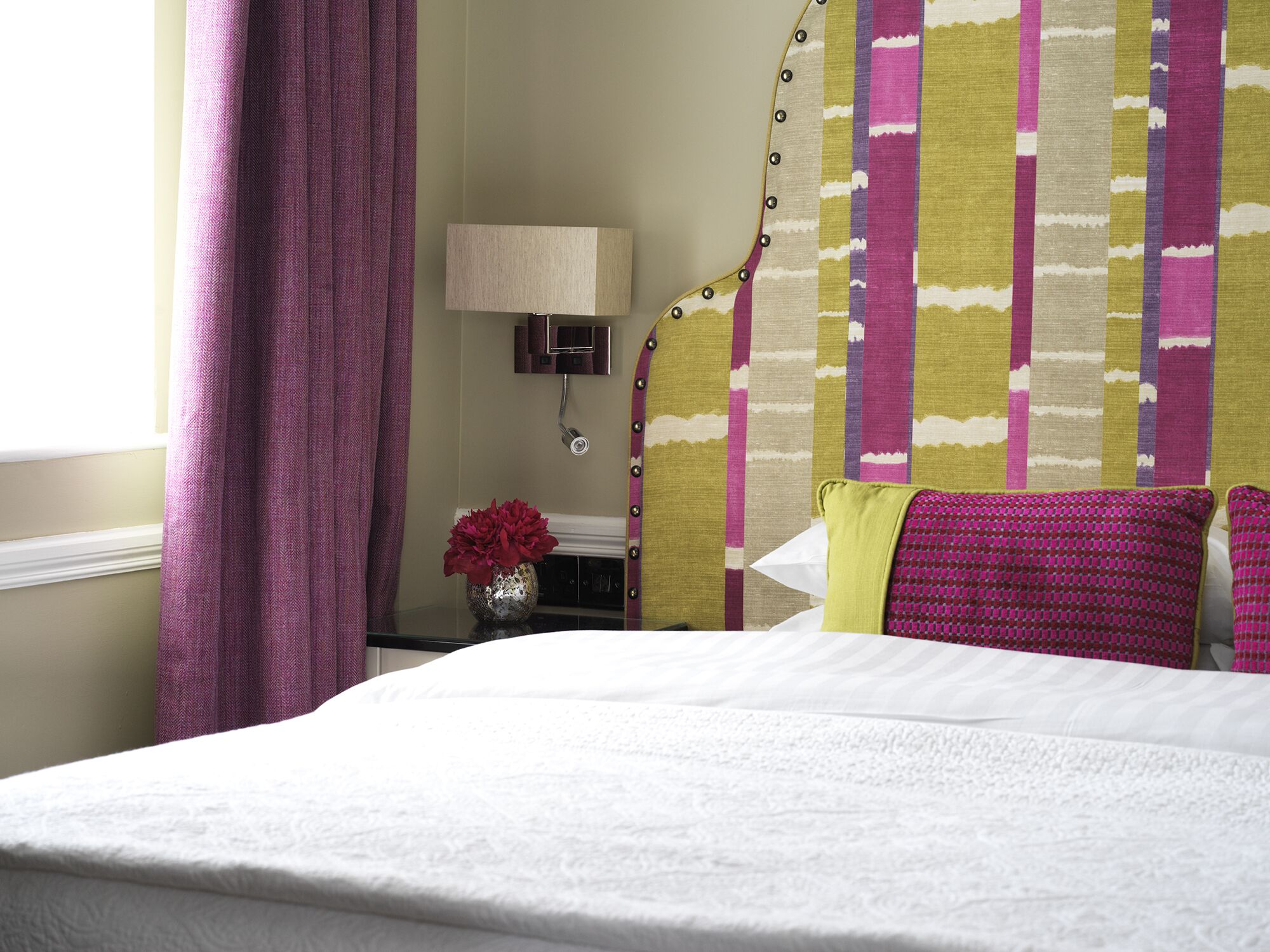 A hotel room with a bed, a nightstand, a lamp, and a wall with a striped pattern.