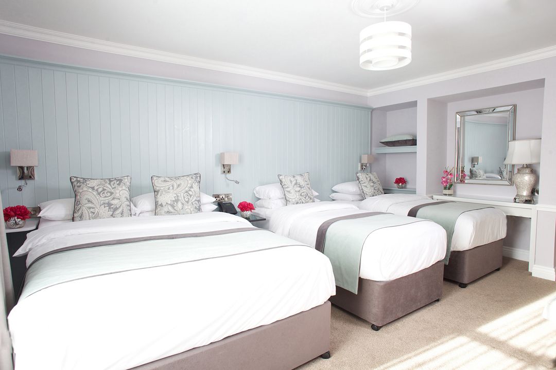 Ein Hotelzimmer mit drei Betten, jeweils mit Kissen und einem Nachttisch mit Lampe.