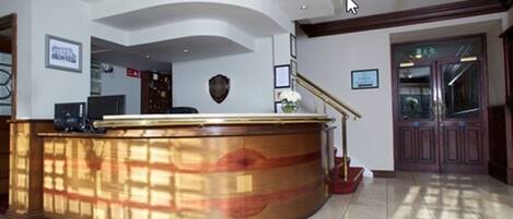 Un área de recepción con un mostrador curvo de madera, un perchero y una escalera que sube a un piso superior.