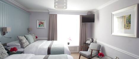 Habitación de hotel con dos camas, un televisor, una silla y una mesita con un florero.