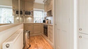 Una cocina compacta con gabinetes de madera, un microondas de acero inoxidable, un horno y un pequeño contenedor de basura.