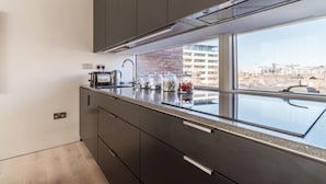 A modern kitchen with dark cabinets, a stainless steel countertop, and a window with a city view. - The Michael Collins Suite - hiphipstay (Dublin)