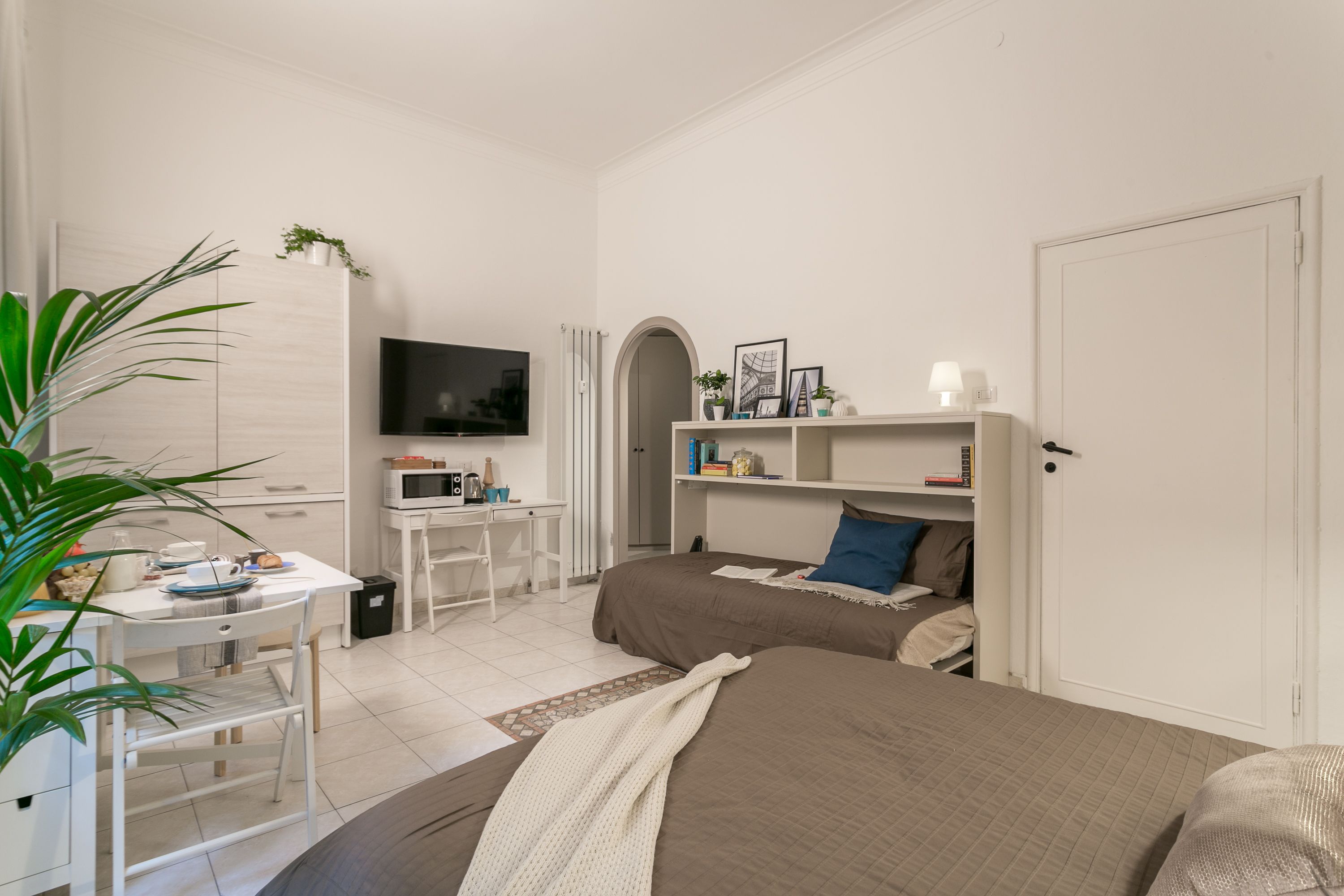 Een moderne slaapkamer met een bed, een bureau, een televisie en een boekenkast.