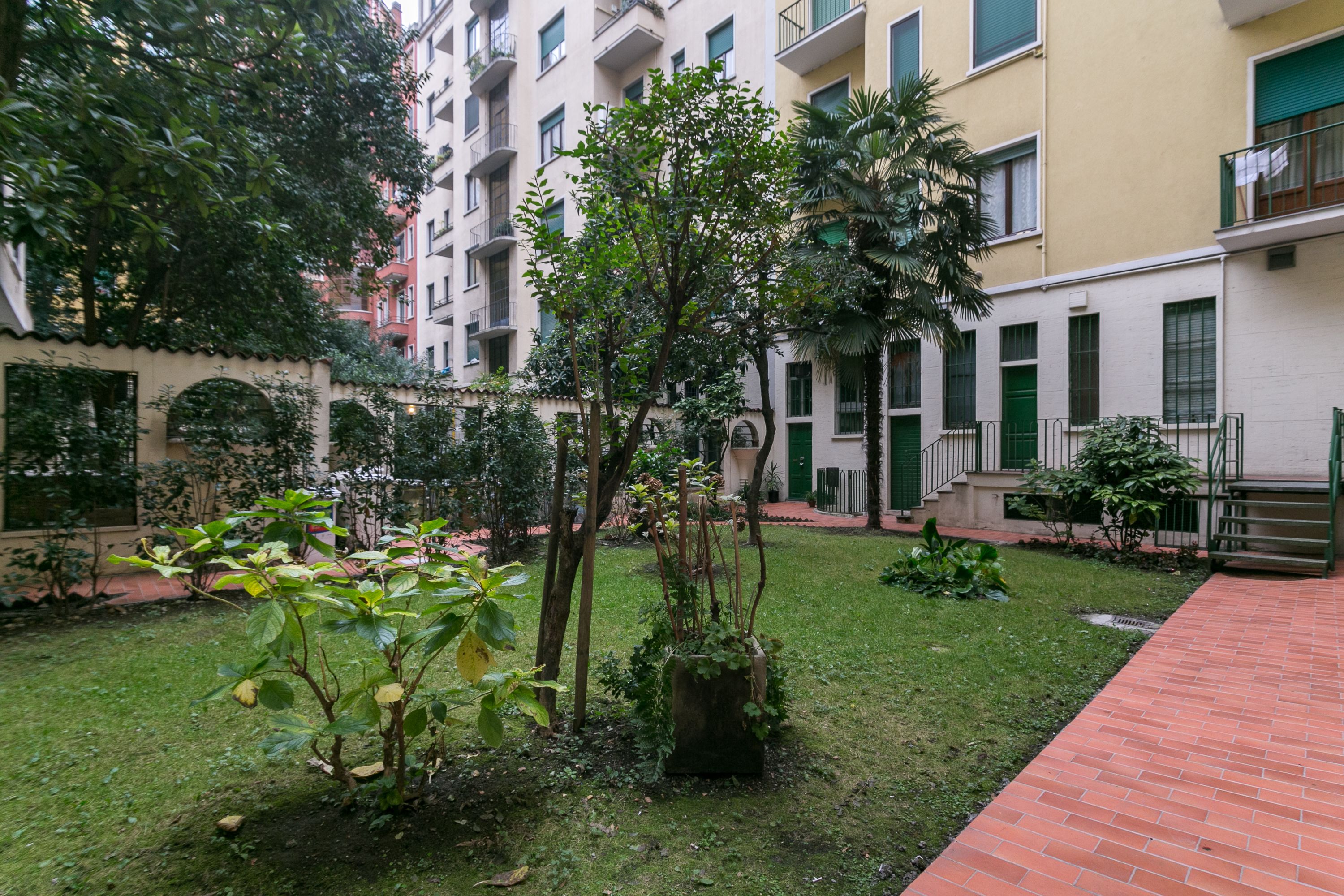 Une cour comprenant une pelouse, un chemin en briques et un petit jardin avec différentes espèces de plantes.