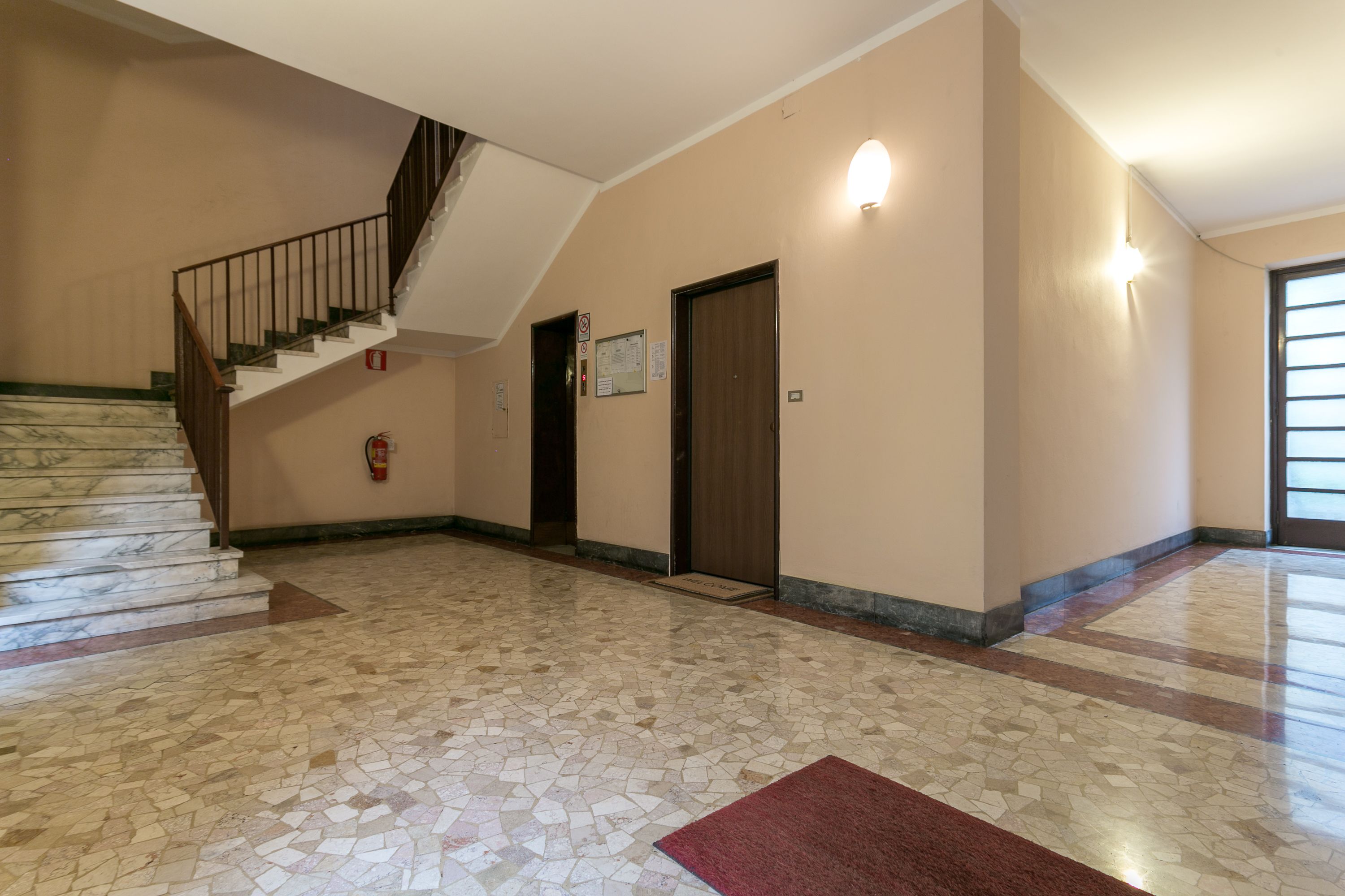 A spacious lobby with a marble staircase, a fire extinguisher, and a door with a sign.