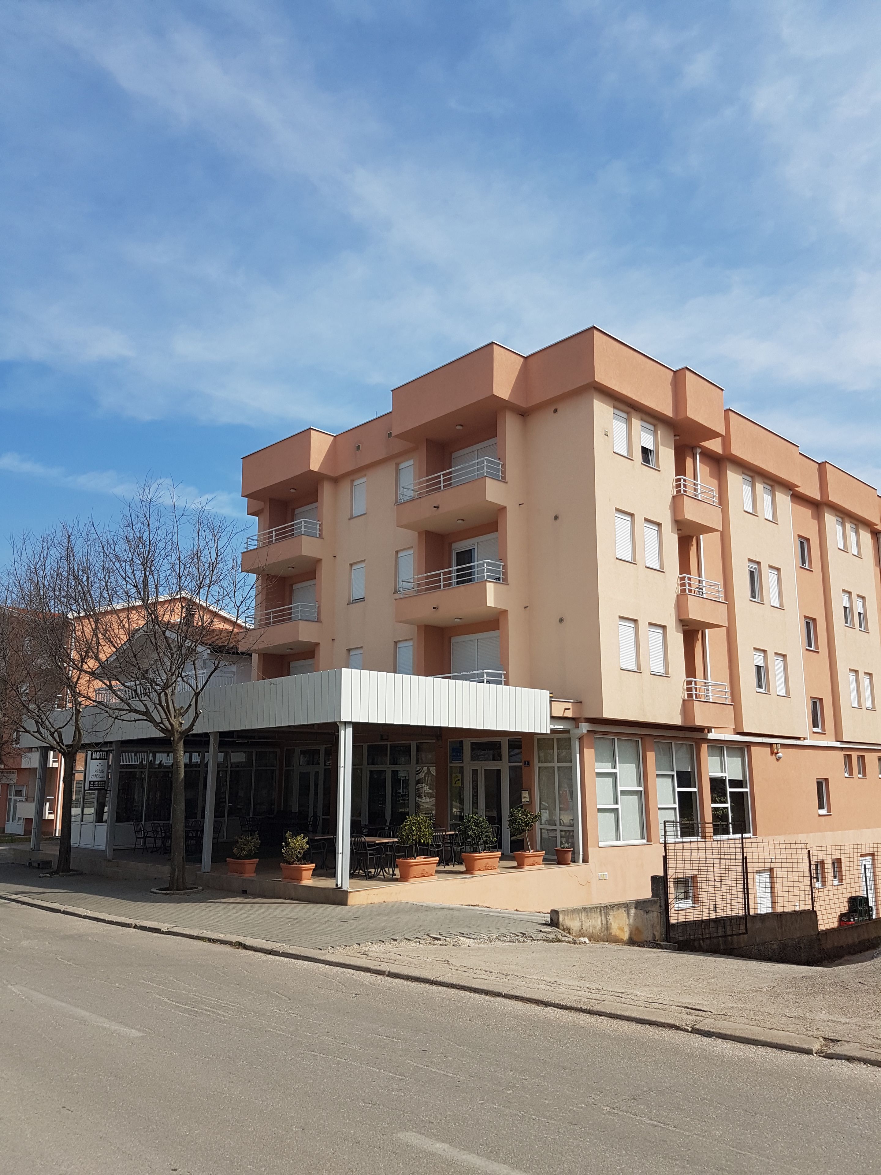 Ein mehrstöckiges Hotel mit Balkonen, einer überdachten Außenbereich-Sitzgelegenheit und Topfpflanzen.