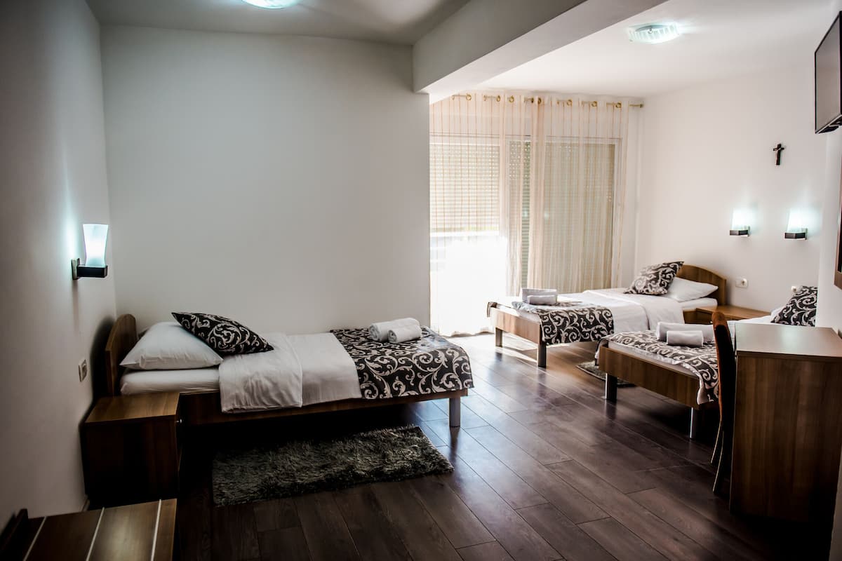 A modern hotel room with two beds, a wooden desk, and a large window with curtains.
