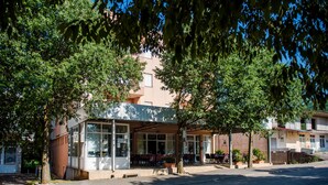A building with a glass facade, outdoor seating, and a tree-lined street.