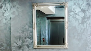 A marble wall with a large mirror and a white bench.
