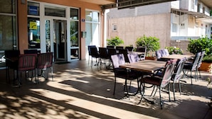 An outdoor patio area with tables and chairs, a reception desk, and potted plants.