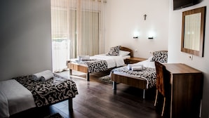 A hotel room with two single beds, a wooden desk, a TV mounted on the wall, and a cross on the wall.