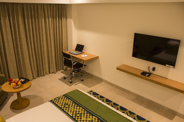 A hotel room with a desk, chair, television, and a bed.