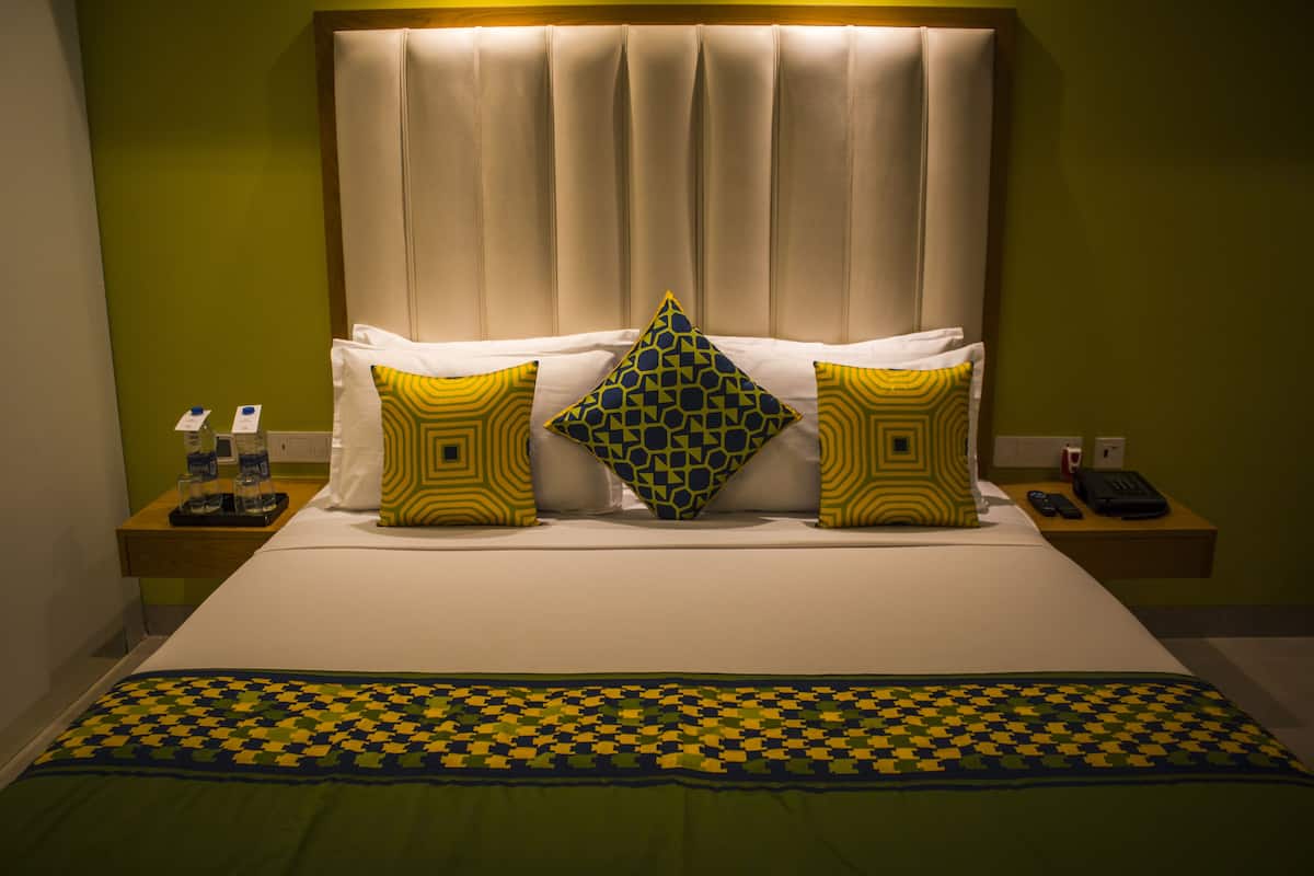 Una habitación de hotel con cama, almohadas, manta, mesita de noche y teléfono.