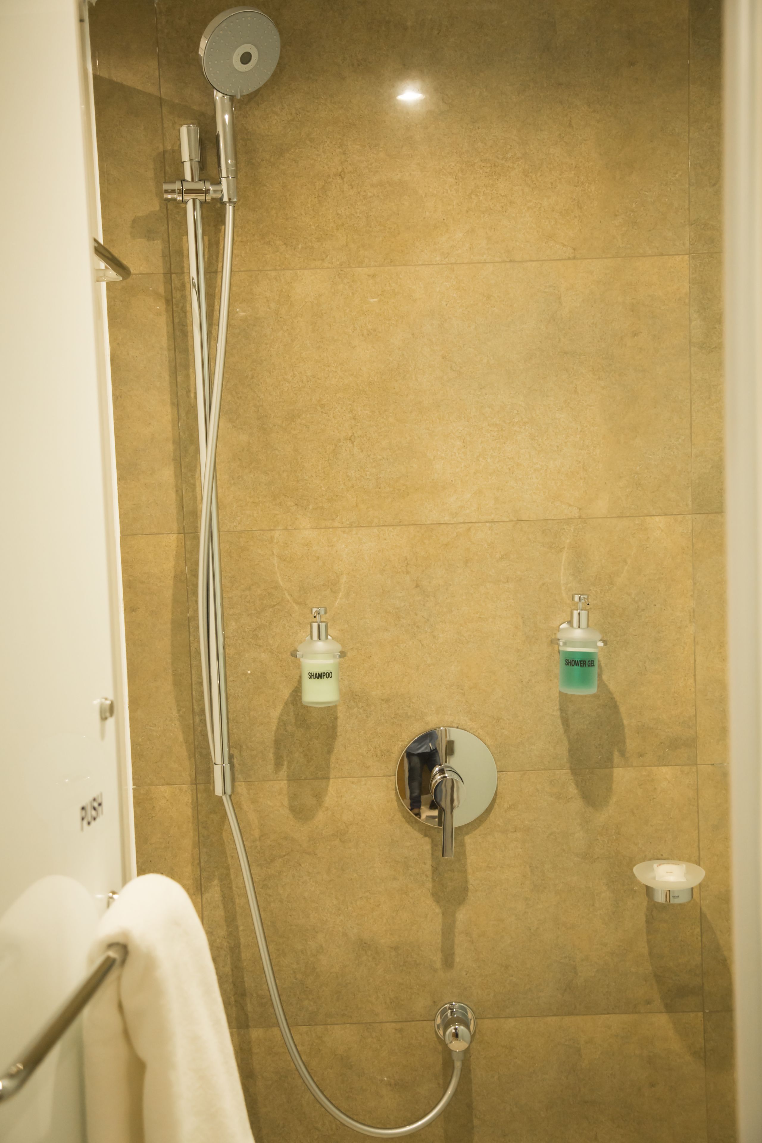 Une douche équipée d’un pommeau de douche à main, d’un robinet mural et de deux distributeurs de savon.