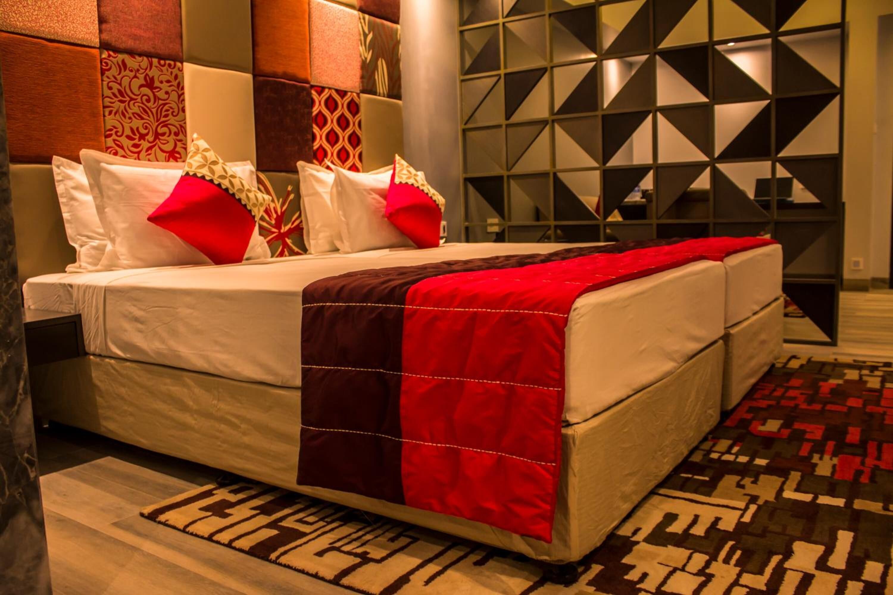 A hotel room with a large bed, a red and white quilt, and a patterned rug.