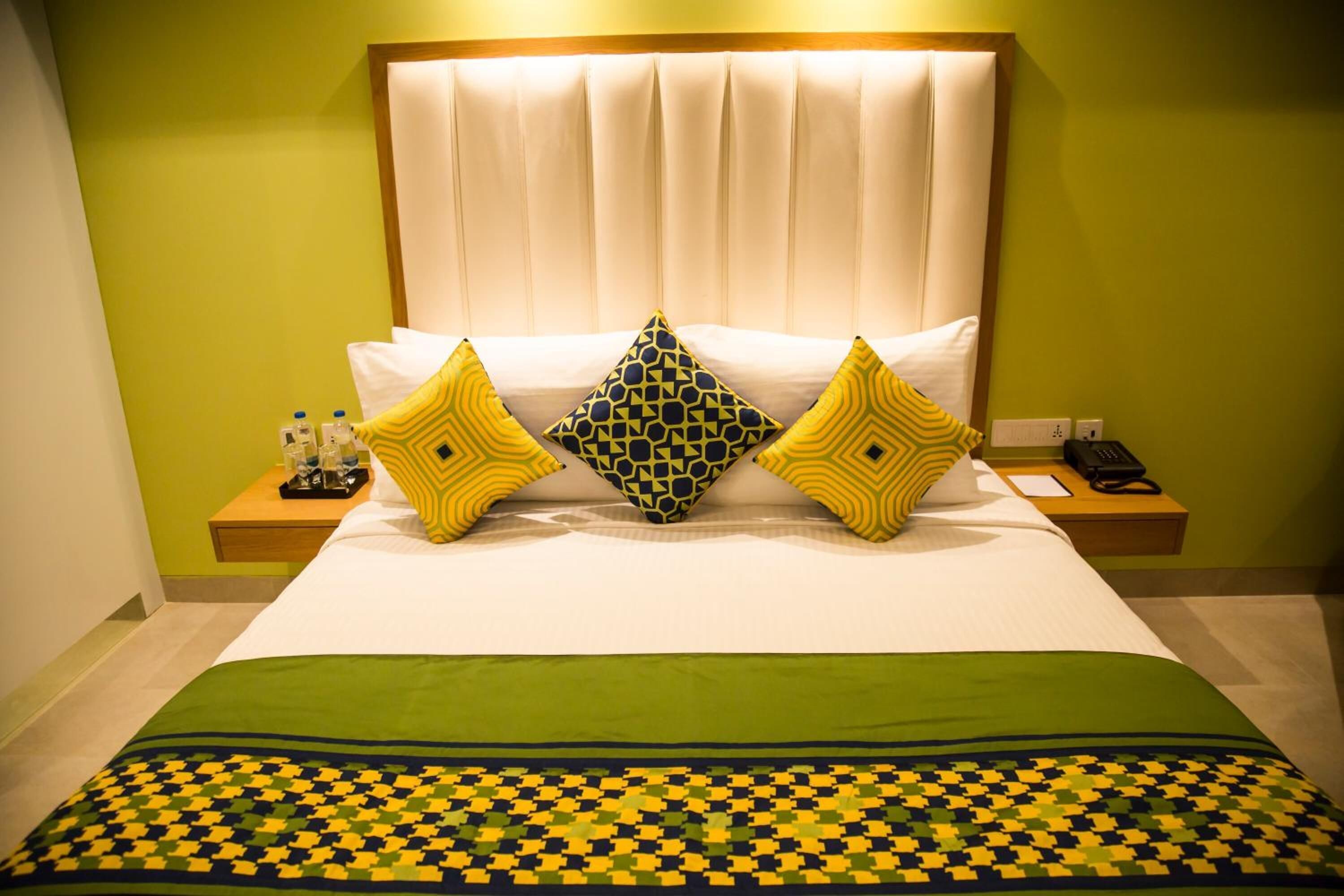 A hotel room with a bed, green walls, a patterned bedspread, and decorative pillows.
