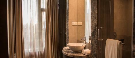 A modern bathroom with a large sink, a glass shower enclosure, and a view of the outdoors through sheer curtains.