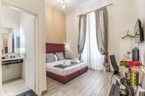 A hotel room with a bed, a bedside table, a mirror, a shower area, and a small table with a vase of flowers. - Operà Suites Roma (Rome)