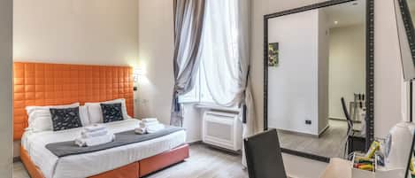 A hotel room with a bed, a chair, a desk, a mirror, and a window with curtains.