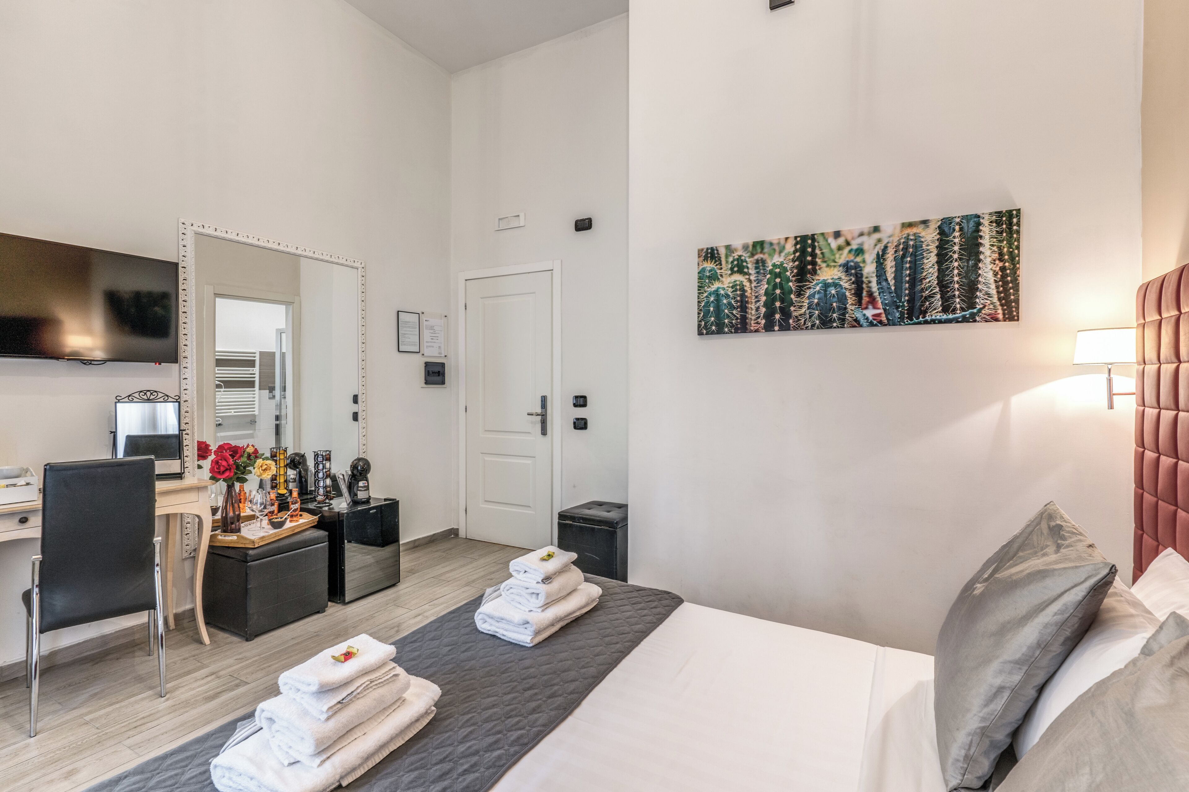 A hotel room with a bed, a desk, a chair, a TV, a door, and a painting on the wall.
