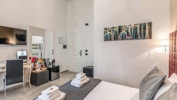 Habitación de hotel con cama, escritorio, silla, televisor, puerta y un cuadro en la pared.