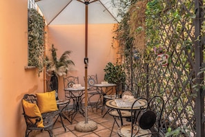 An outdoor patio with round tables and chairs, a central umbrella, and a decorative fence with climbing plants. - Operà Suites Roma (Rome)