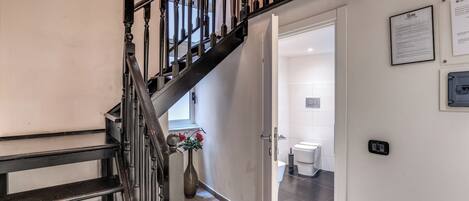 A staircase with a wooden handrail and black balusters leading to a room with a toilet and a sink.