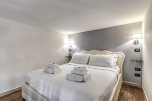 A neatly made bed with white linens and towels, a headboard, bedside lamps, and a wooden floor. - Operà Suites Roma (Rome)