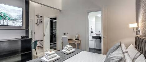 A hotel room with a bed, a desk, a chair, a TV, and a bathroom visible through an open door.
