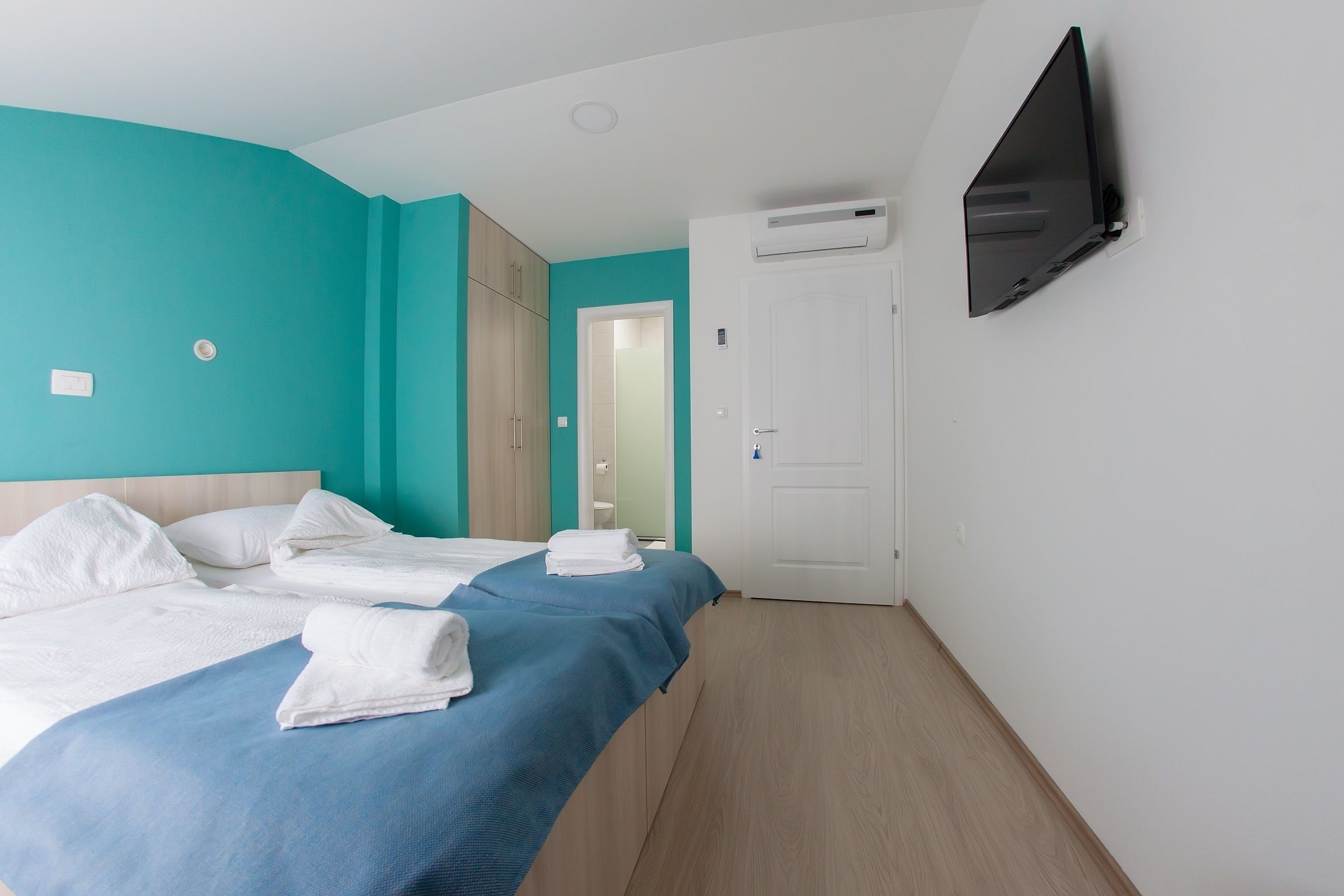 A hotel room with a bed, a TV mounted on the wall, and an air conditioning unit.