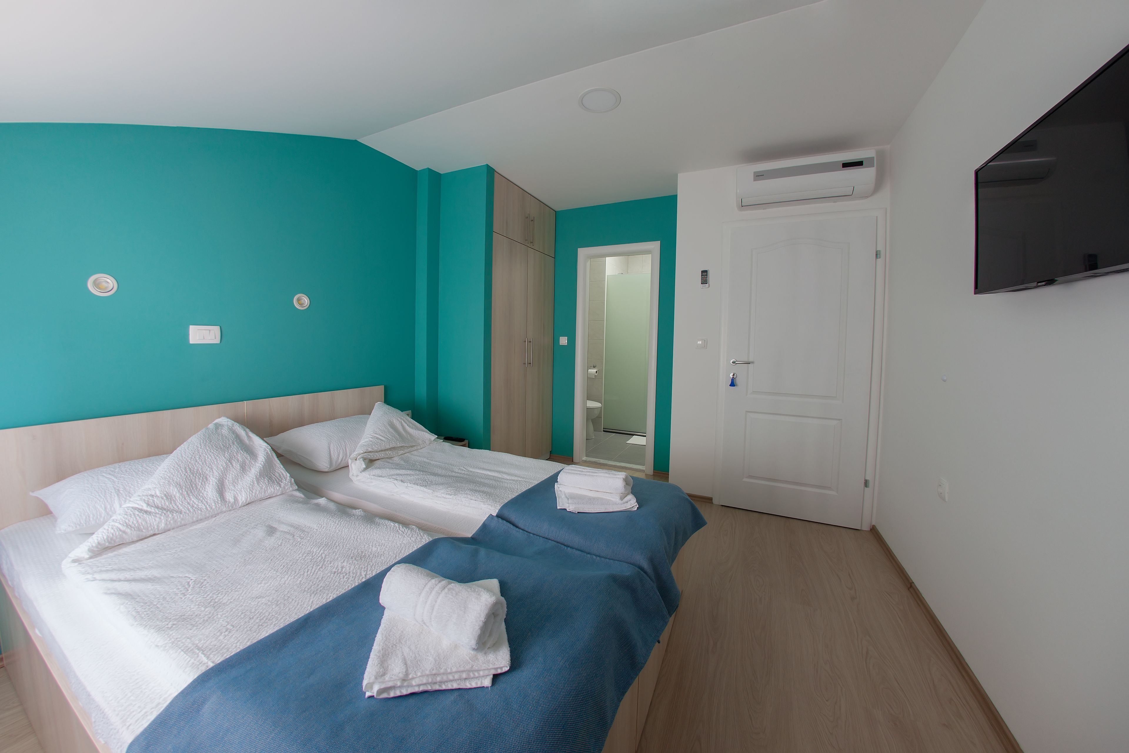 Quarto de hotel com duas camas, paredes verde-água, porta branca e televisão na parede.