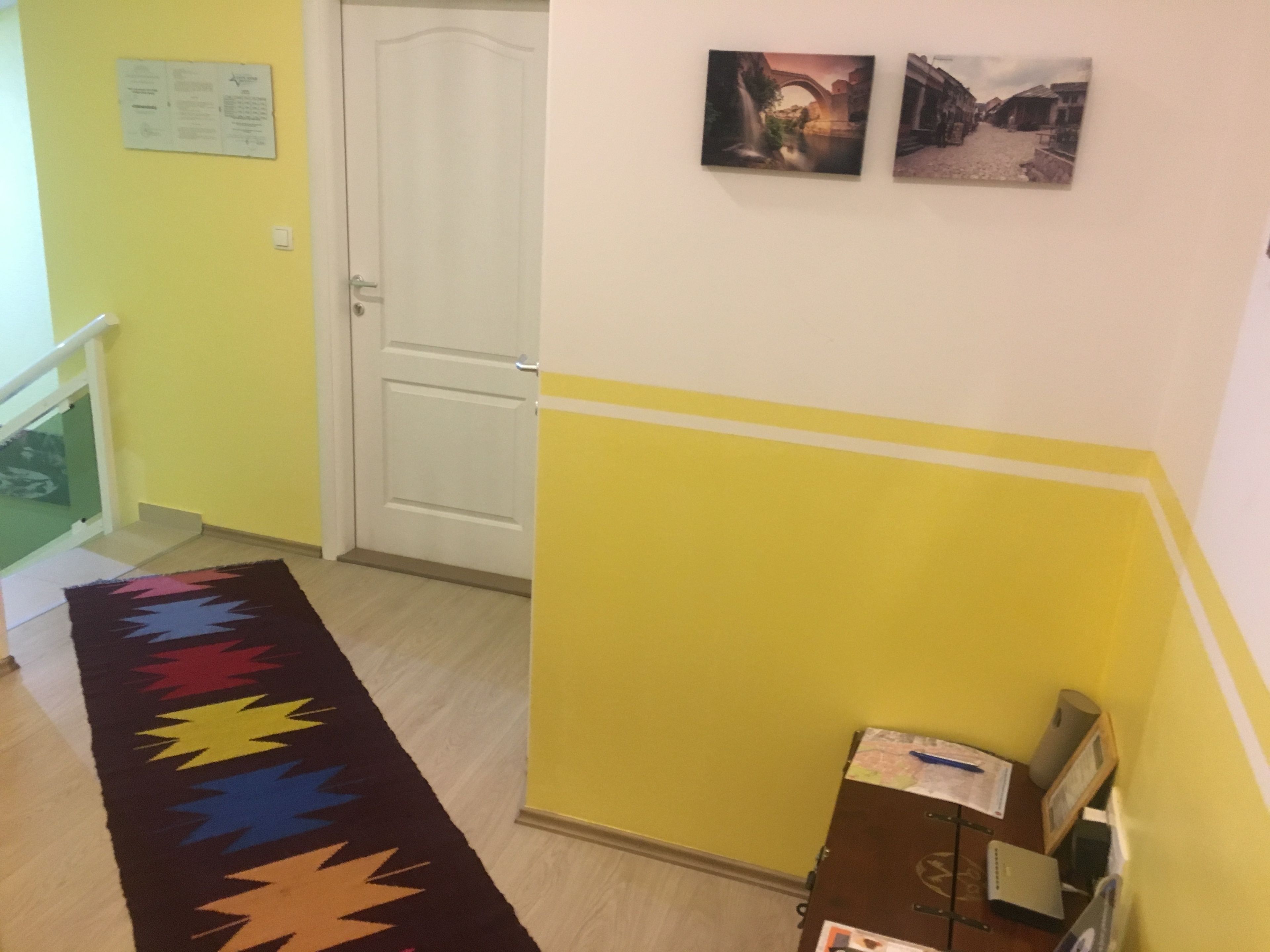 Um corredor com um tapete colorido, uma porta e duas imagens emolduradas na parede.