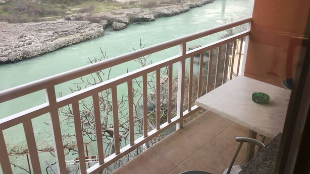 A balcony with a view of a river, a table, and a chair. - Guest House City Star (Mostar)