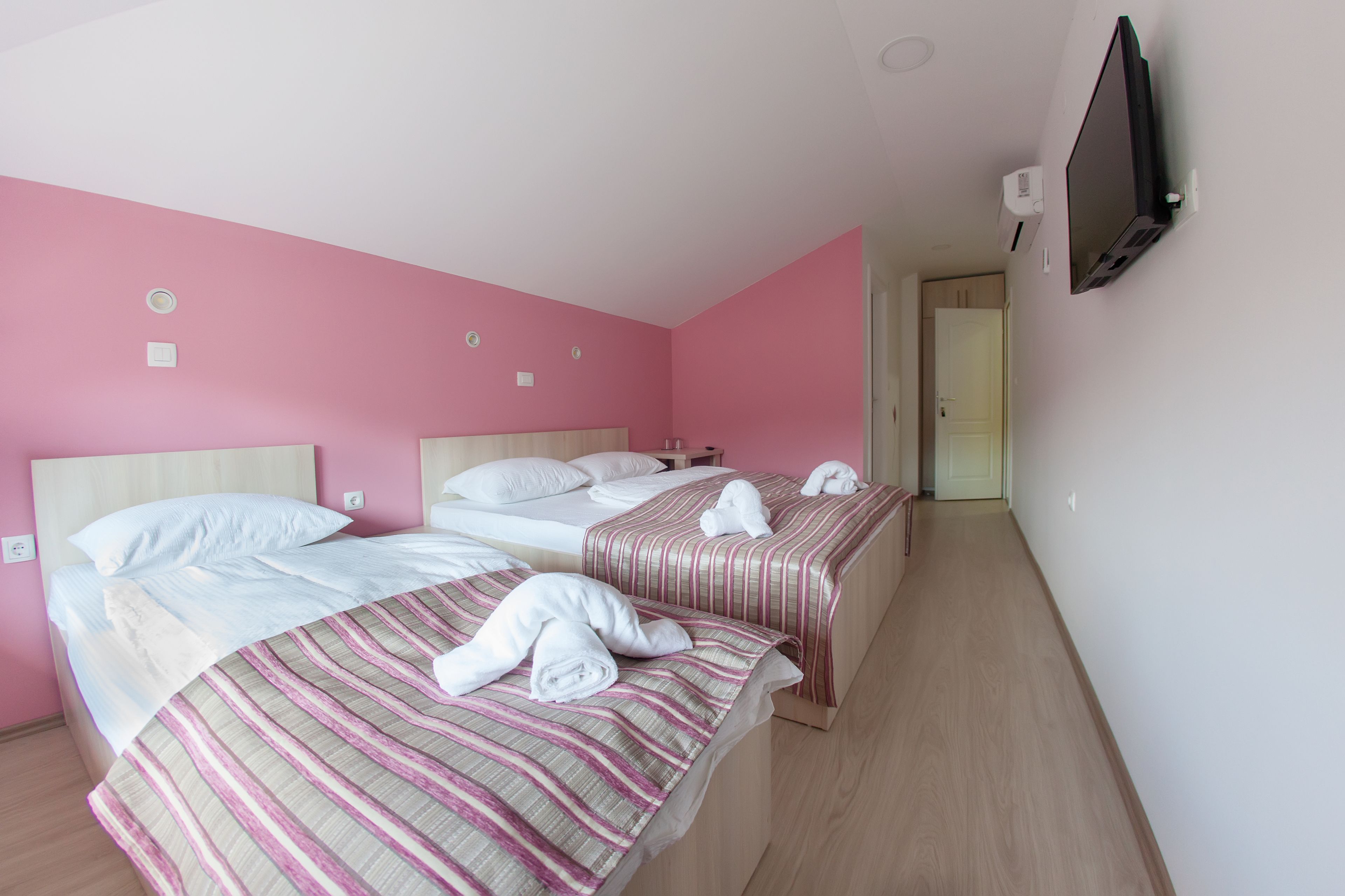Ein Hotelzimmer mit zwei Betten, rosafarbenen Wänden und einem an der Wand befestigten Fernseher.
