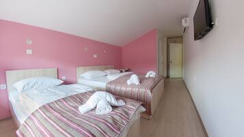 Ein Hotelzimmer mit zwei Betten, rosafarbenen Wänden und einem an der Wand befestigten Fernseher.