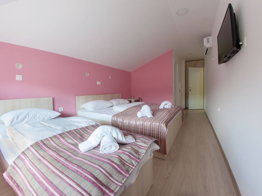 Ein Hotelzimmer mit zwei Betten, rosafarbenen Wänden und einem an der Wand befestigten Fernseher.