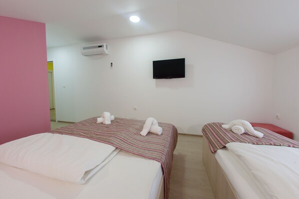Una habitación con dos camas, cada una con colcha a rayas y almohadas blancas, un televisor de pantalla plana montado en la pared y un equipo de aire acondicionado.
