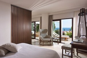 Habitación de hotel con cama, una silla, una mesa con una computadora portátil y vista al mar.