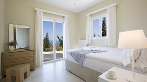 A bedroom with a bed, a bedside table, a lamp, a dresser, a mirror, and a view of the outdoors. - Boo Premium Living Villas (Lefkada)